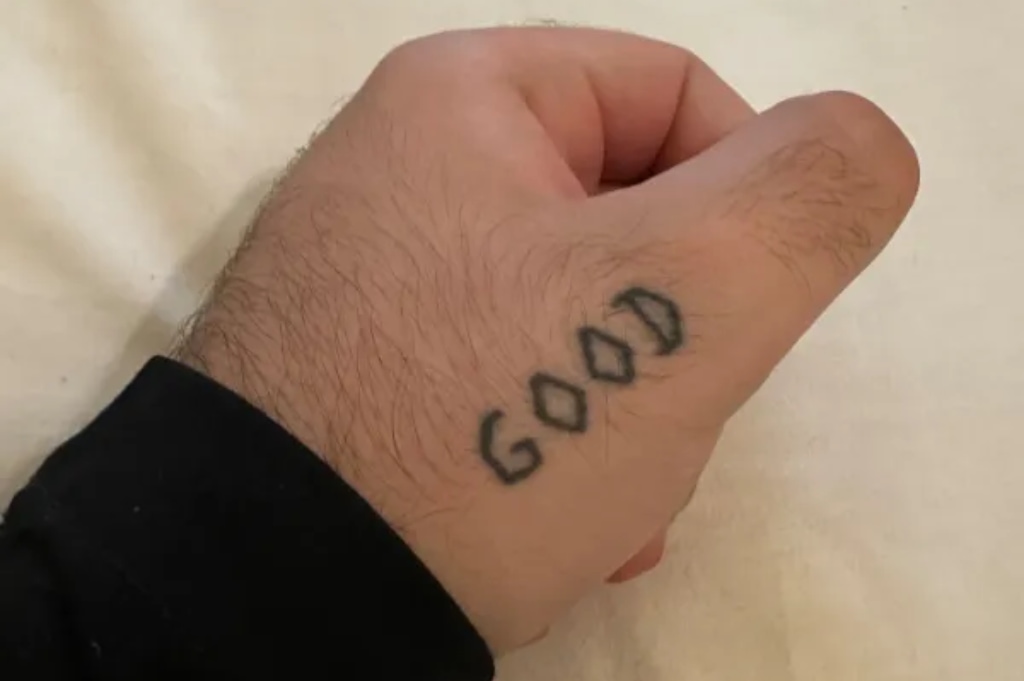 Dedo polegar esquerdo com uma tatuagem escrita 'GOOD'.