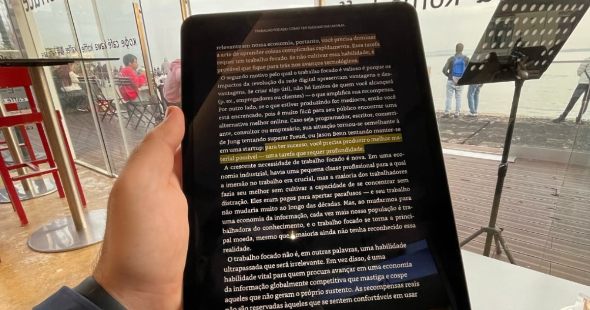 iPad sendo segurando pela minha mão esquerda. Ao fundo, um café em Lisboa, Portugal.